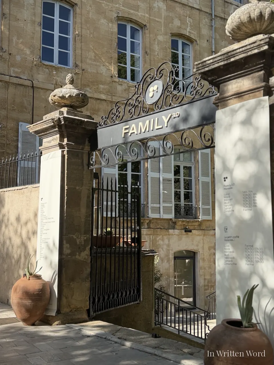 A wrought-iron gate with the Family 3.0 sign, framed by stone pillars and terracotta urns, in front of a historic stone building in Aix-en-Provence.