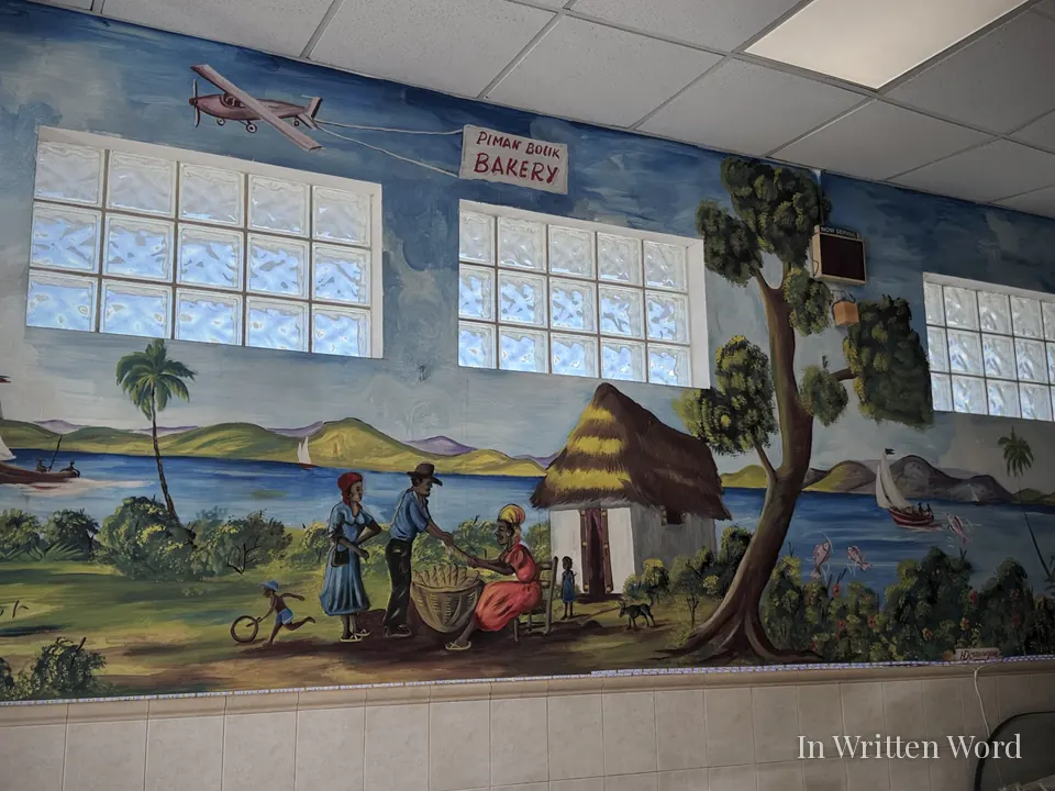 Colorful mural inside Piman Bouk Bakery in Little Haiti, Miami, depicting a Haitian coastal village scene with people, boats, mountains, and a thatched-roof house.